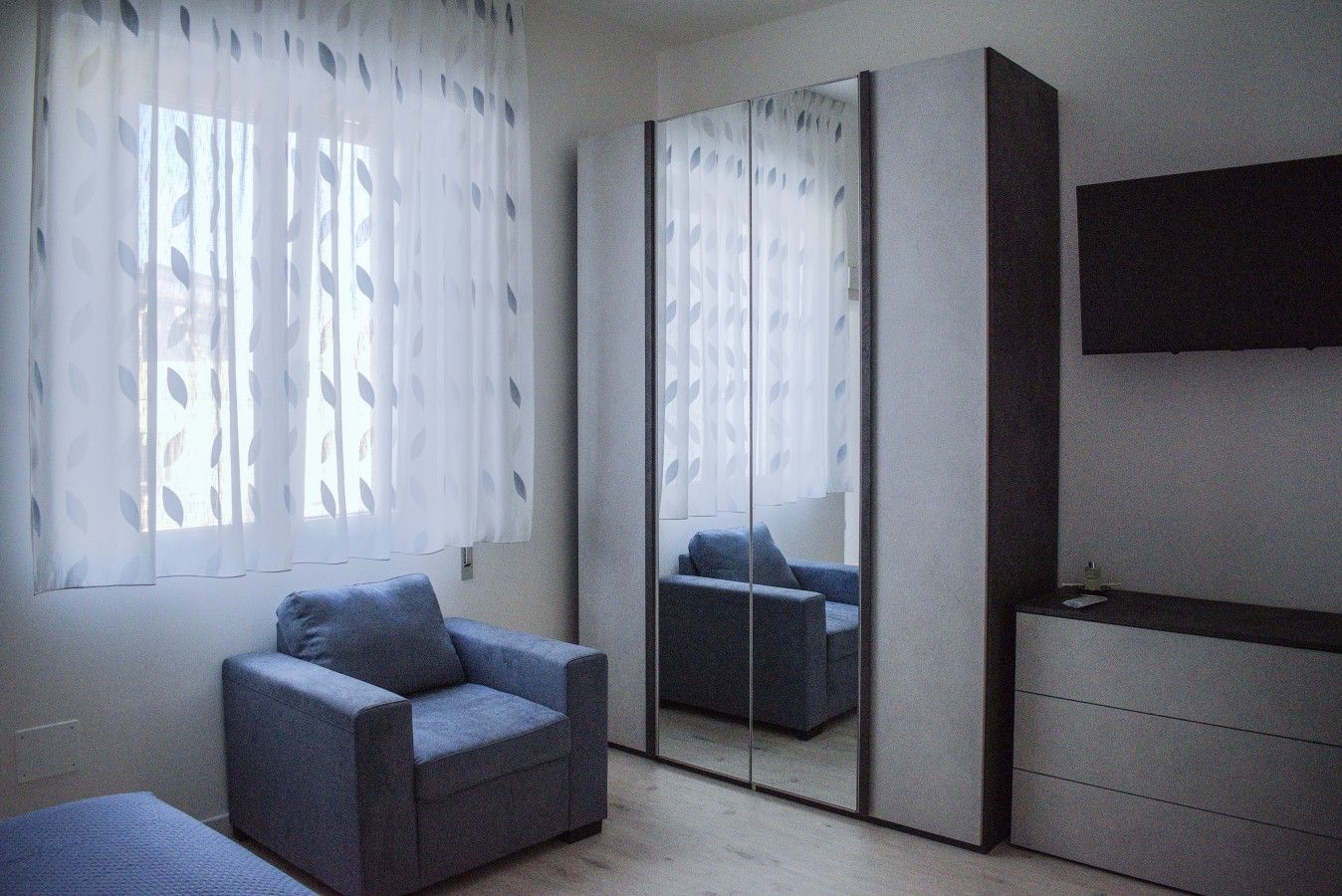 Une chambre avec un lit simple, une chaise, une armoire et un miroir.