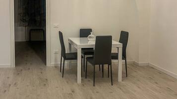 A dining area with a white table and four chairs, a glass-top table, and a door leading to another room.