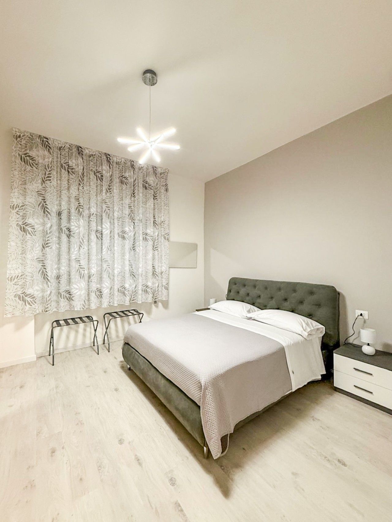 A bedroom with a bed, bedside table, lamp, and a window with curtains.