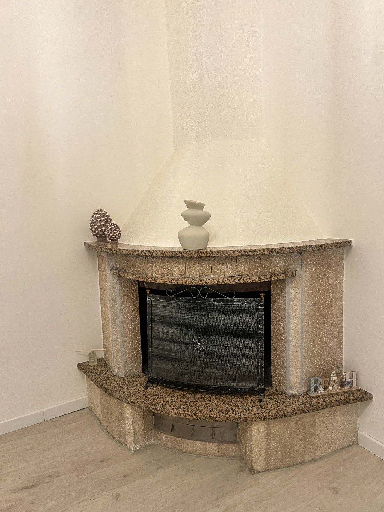A fireplace with a stone surround, a decorative vase, and a pine cone on the mantel.