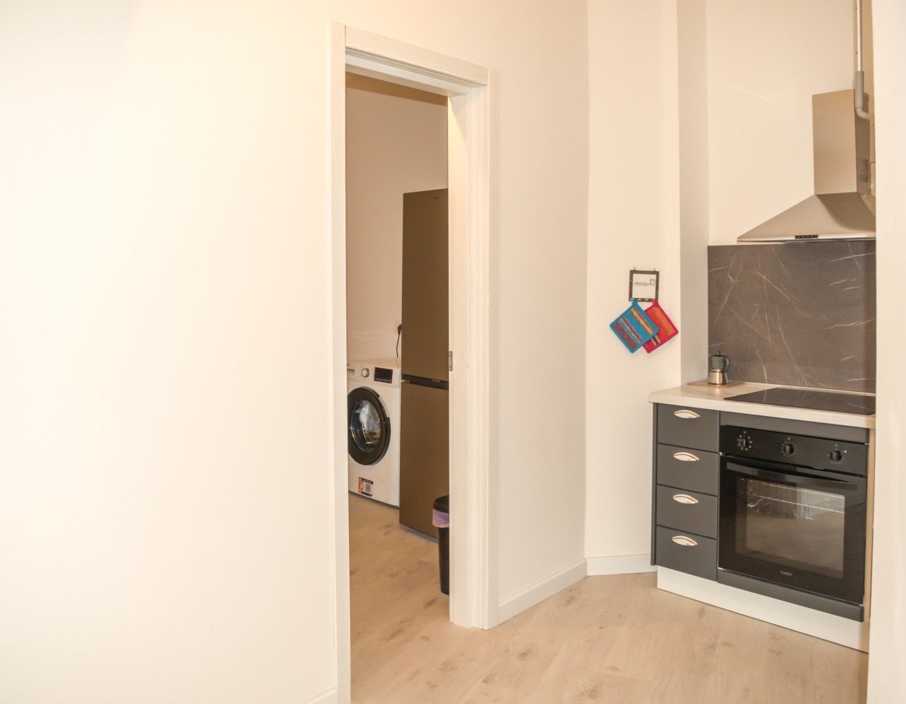 A compact kitchen with a built-in oven and a washing machine in the adjacent room.