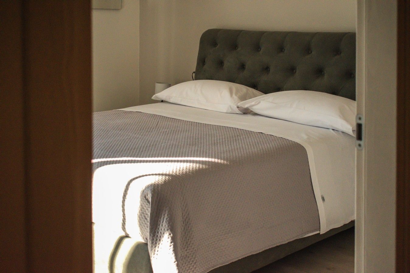 Ein Schlafzimmer mit einem Bett, einem grauen gepolsterten Kopfende und weißer Bettwäsche.