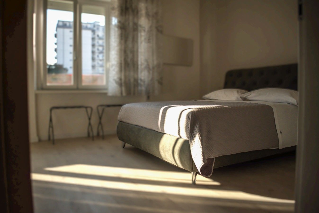 A bedroom with a bed, a window, and a view of buildings outside.
