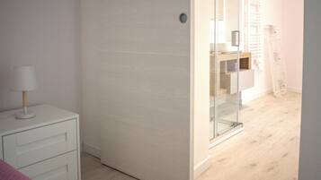 A room with a white bedside table, a lamp, a mirror, and a wooden floor.
