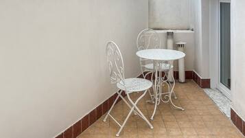 Eine kleine Außenveranda mit weißem Tisch und Stühlen, einer weißen Badewanne und einem gefliesten Boden.