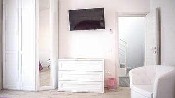 Ein Schlafzimmer mit weißem Kleiderschrank, einem Nachttisch, einem an der Wand befestigten Fernseher und einer rosa Bettdecke.