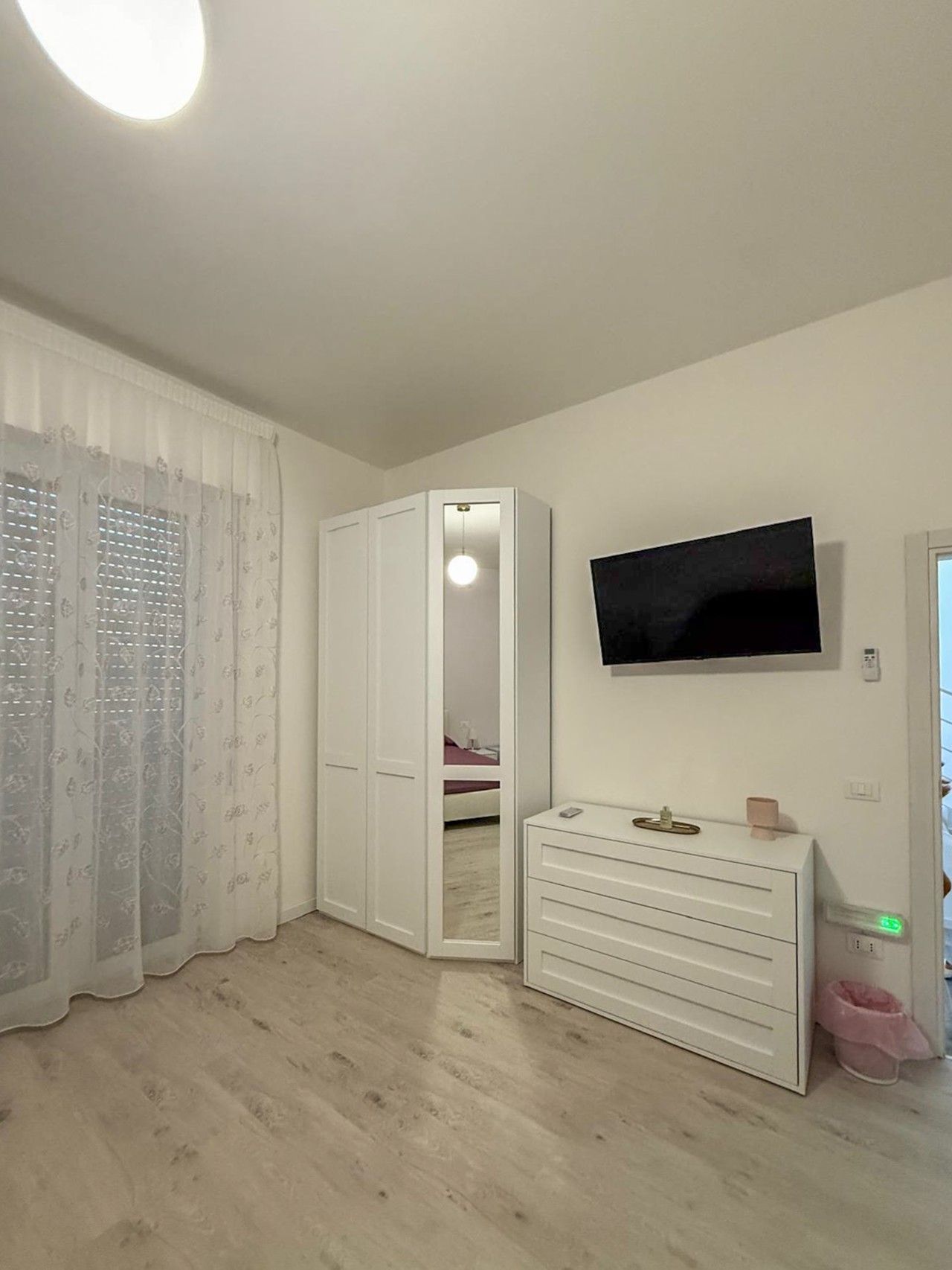 A bedroom with a bed, a wardrobe, a dresser, a television, and a window with curtains.