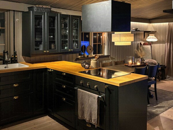 A modern kitchen with dark cabinetry, a wooden countertop, and a built-in stove.