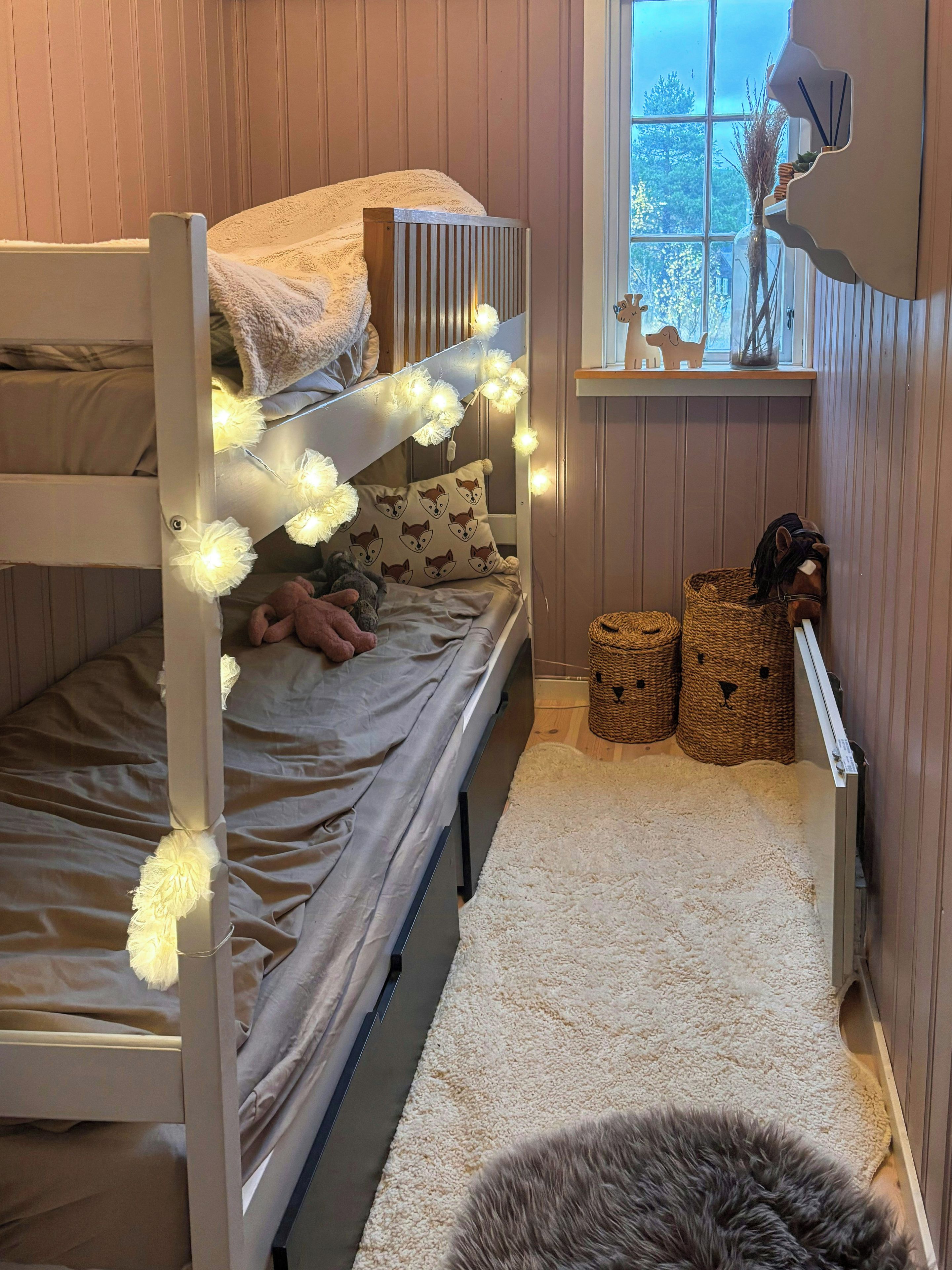 A bunk bed with fairy lights, a plush toy, and a window with a view.