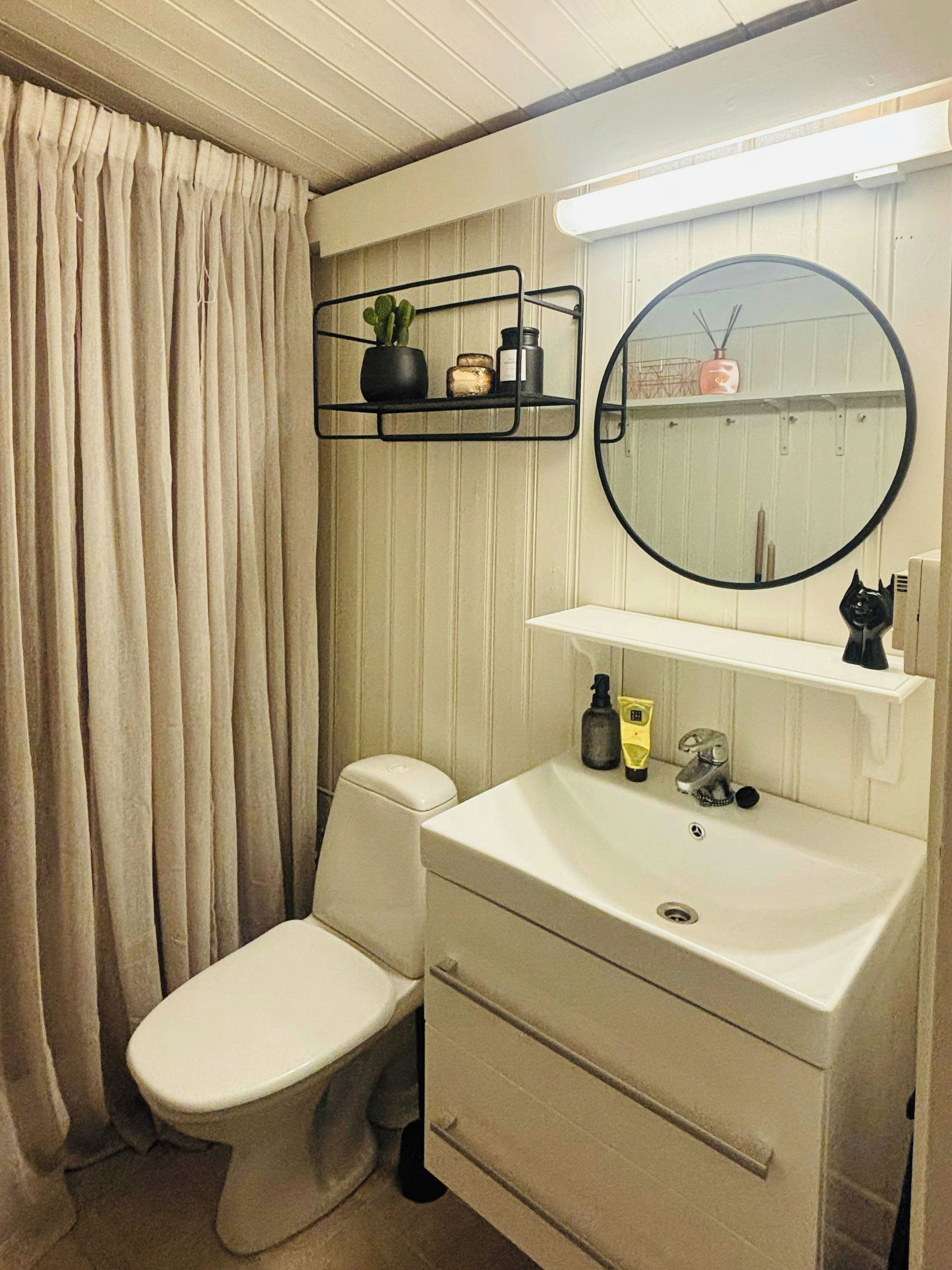 A bathroom with a toilet, a sink with a mirror, and a shelf with toiletries.