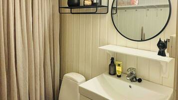 A bathroom with a toilet, a sink with a mirror, and a shelf with toiletries.