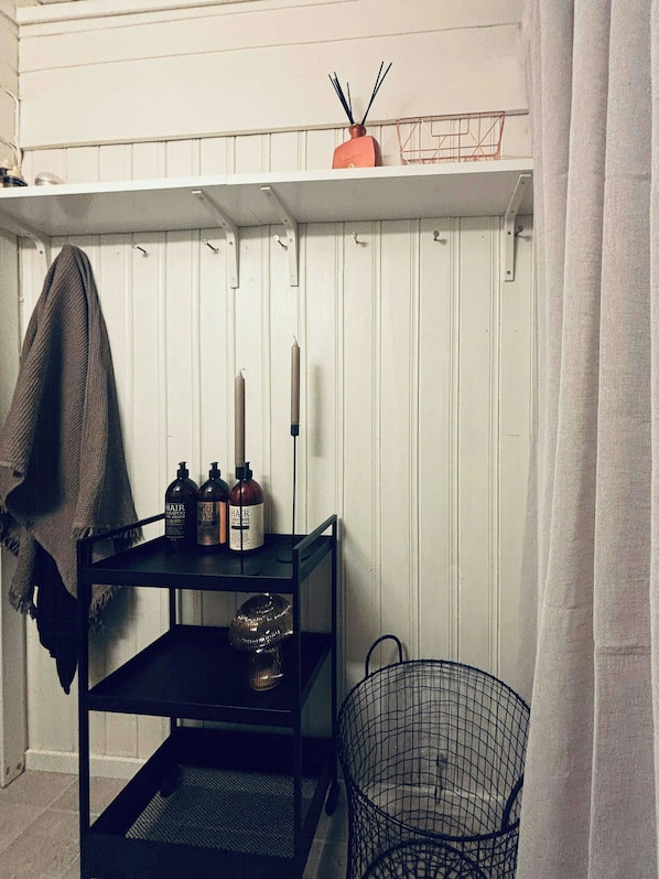 Ein Zimmer mit einer weißen Wand, einem schwarzen Regal mit Haarpflegeprodukten, einer Kerze und einem Drahtkorb.