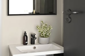 Een badkamer met een wit wastafel, een zwarte zeepdispenser en een potplant.