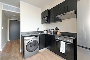 Une cuisine compacte équipée d’un lave-linge, d’un four, d’un four à micro-ondes et d’une plaque de cuisson intégrée.
