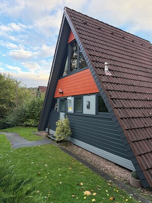A modern house with a sloped roof, a small front yard, and a pathway leading to the entrance. - Lavendel Vacation Home with a Large Terrace. Centrally located in the Machtlos Vacation Park (Ronshausen)