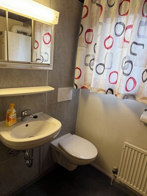 A bathroom with a sink, toilet, and a shower curtain with a geometric pattern. - Lavendel Vacation Home with a Large Terrace. Centrally located in the Machtlos Vacation Park (Ronshausen)