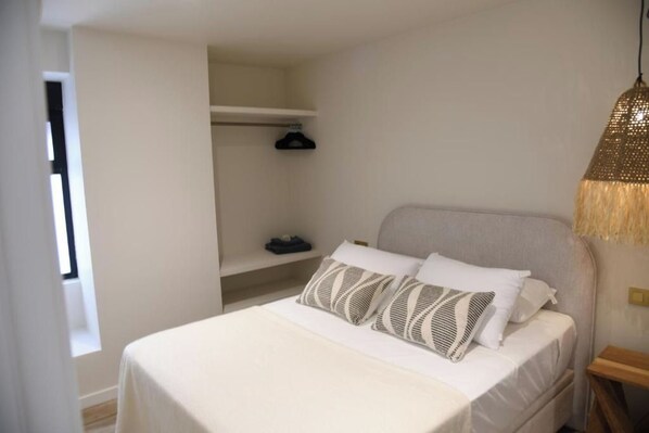 A bedroom with a bed, a hanging light fixture, and a shelf with a hanger.