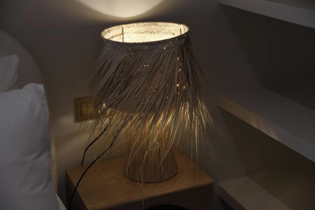 Una lámpara con pantalla tejida sobre una mesita de noche de madera.