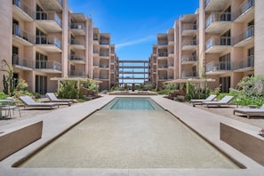 A pool area with lounge chairs and a clear view of the building's architecture. - Cabo Getaway · 2BR · Pool + Jacuzzi · Near Beach (Cabo San Lucas)