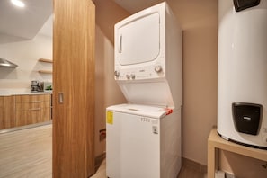 A compact kitchen with a built-in washer and dryer, wooden cabinets, and a coffee machine. - Cabo Getaway · 2BR · Pool + Jacuzzi · Near Beach (Cabo San Lucas)