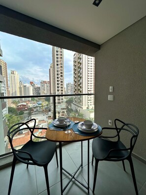 A balcony with a table set for two, overlooking a cityscape with high-rise buildings. - Level Brooklin 1007 (São Paulo)