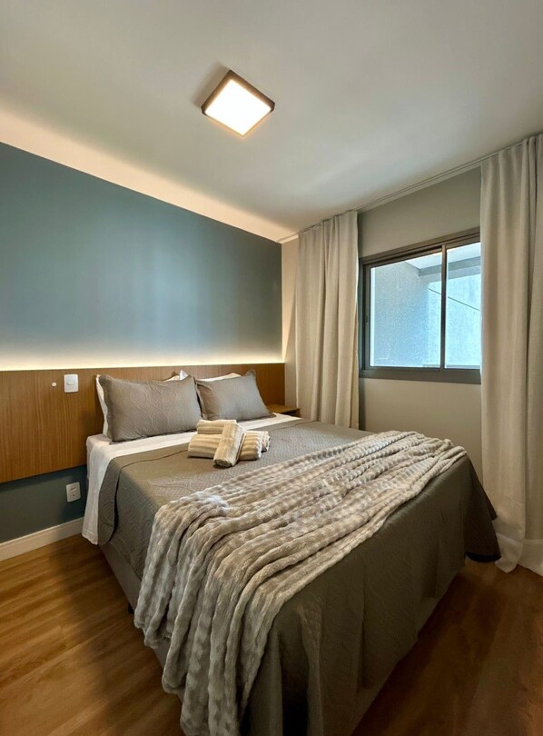 Ein Schlafzimmer mit einem Bett, einem Nachttisch, einem Fenster mit Vorhängen und einer Deckenleuchte.