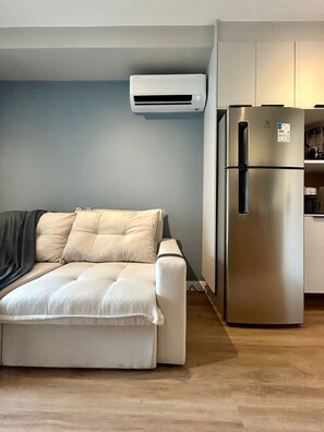 Ein kompakter Wohnraum mit einer Couch, einer eingebauten Klimaanlage und einem Edelstahl-Kühlschrank.