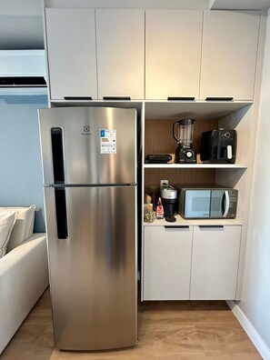 A compact kitchen with a stainless steel refrigerator, a microwave, and a coffee maker on the countertop. - Level Brooklin 1007 (São Paulo)