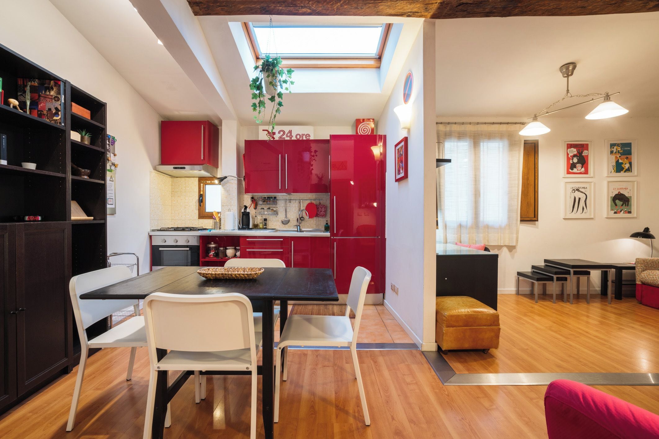 A compact kitchen with red cabinets, a dining table with chairs, and a skylight above.