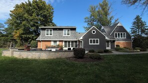 A two-story house with a stone retaining wall, a patio with outdoor furniture, and a large tree in the background. - Spacious 5-bedroom house in tranquil Princeton (Princeton)