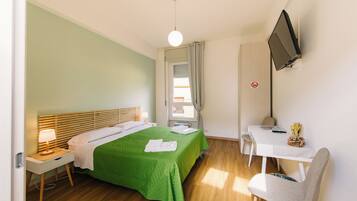 Une chambre d’hôtel équipée d’un lit, d’un bureau, d’une chaise, d’une télévision et d’une fenêtre avec des rideaux.