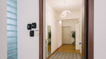 Un couloir doté d’un sol à motifs, une porte avec une poignée moderne et un luminaire au plafond.