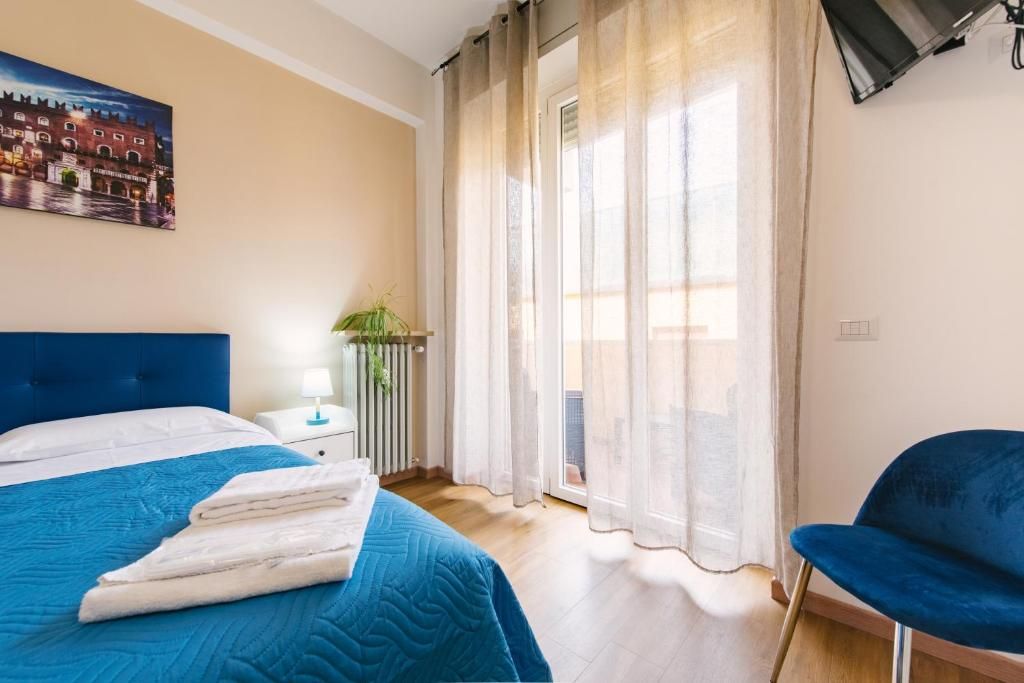 Une chambre d’hôtel avec un lit, une chaise, un radiateur, une fenêtre avec des rideaux et un tableau au mur.
