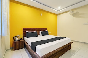 Een hotelkamer met een houten hoofdeinde, een bed met zwart-wit beddengoed, een nachtkastje met een lamp, een dienblad met een koffiezetapparaat en een wandairconditioner.