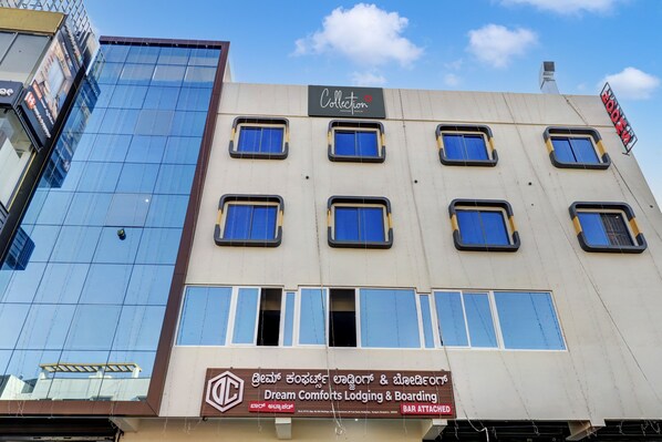 A building with multiple windows, some of which are boarded up. There is a sign for 'Dream Comforts Lodging & Boarding' with a bar attached.