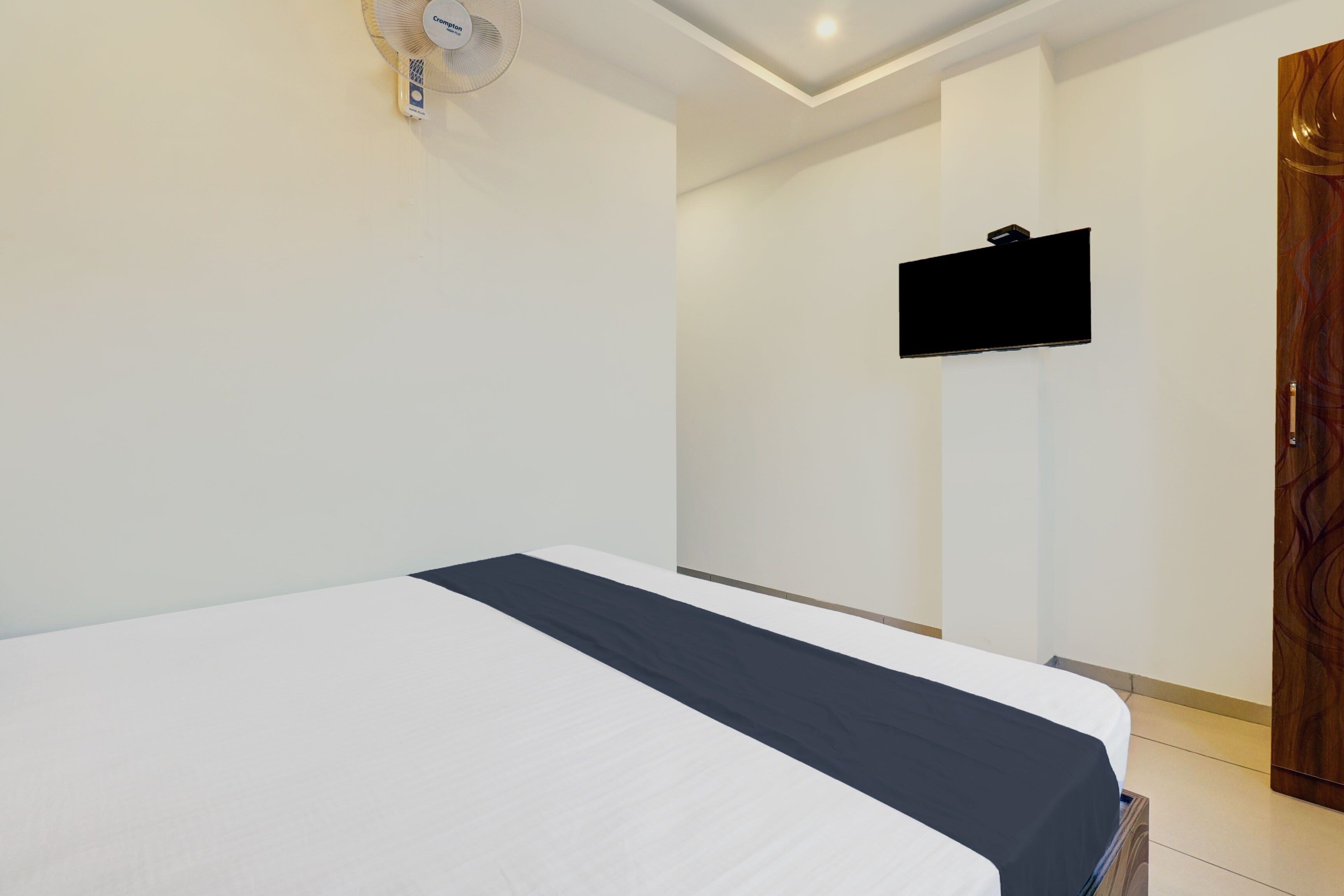 A hotel room with a bed, a flat-screen TV mounted on the wall, and a wooden wardrobe.