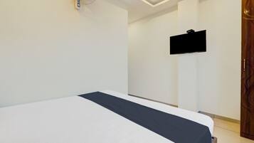 A hotel room with a bed, a flat-screen TV mounted on the wall, and a wooden wardrobe.