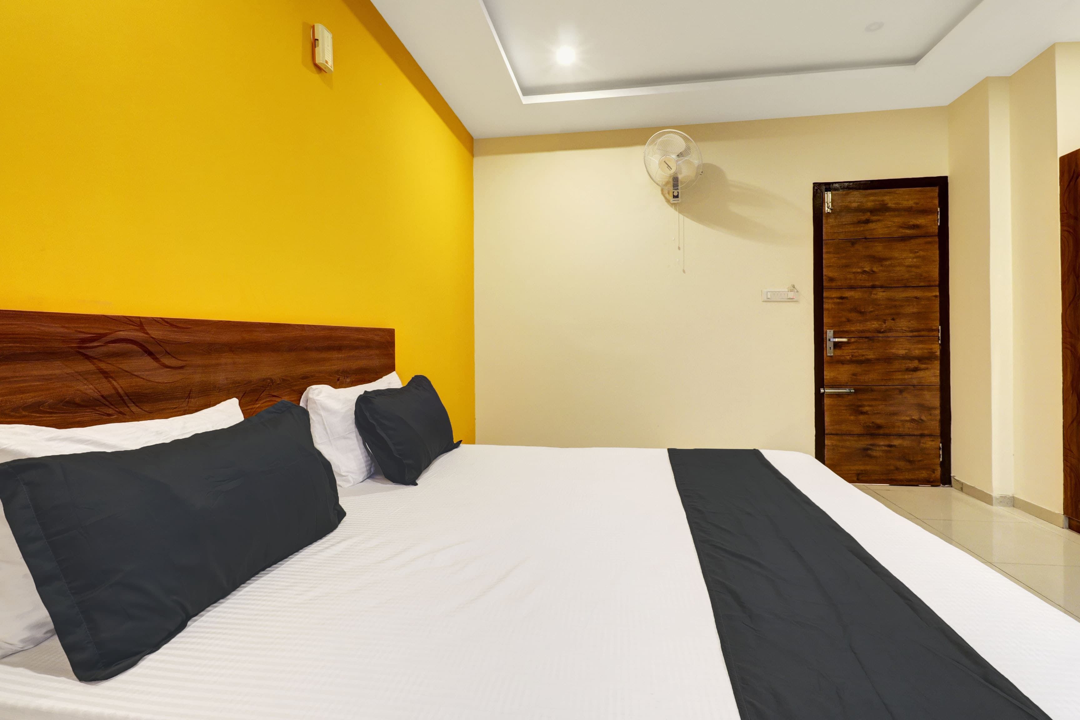 A hotel room with a large bed, a wooden door, and a ceiling fan.