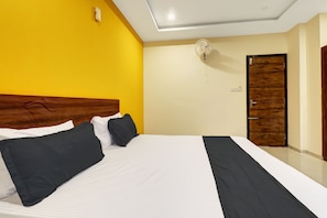 Een hotelkamer met een groot bed, een houten deur en een plafondventilator.