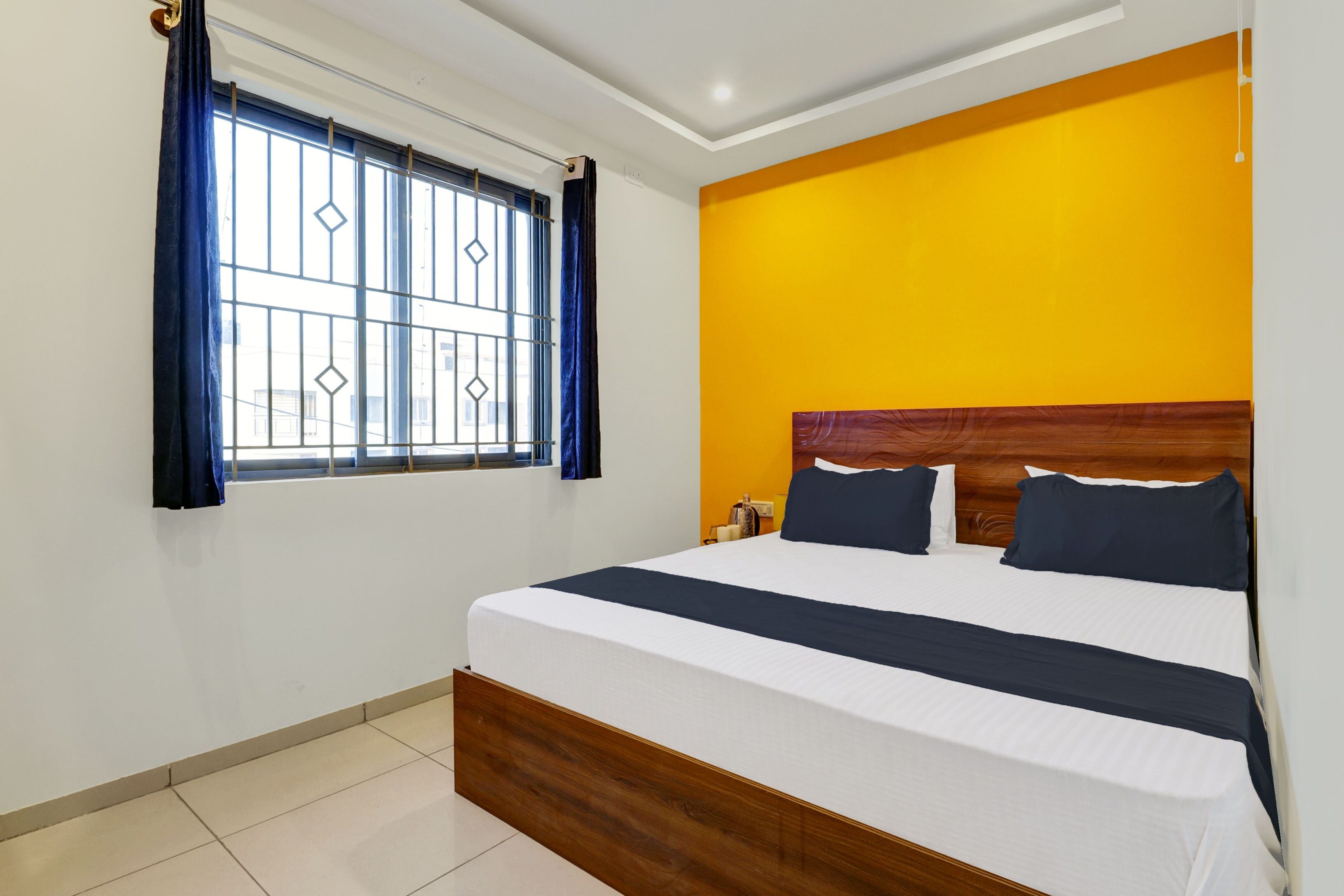 Una habitación de hotel con una cama, un ventanal con cortinas y una pared de acento en color amarillo.