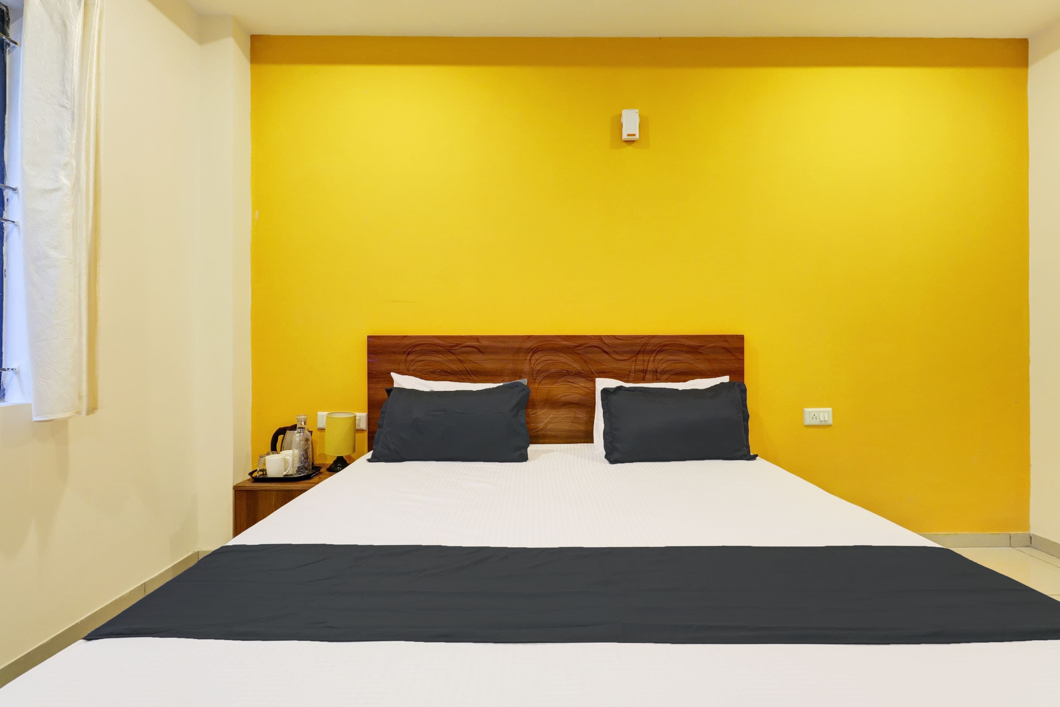 Une chambre d’hôtel avec un grand lit, deux oreillers, une table de chevet avec une lampe et une fenêtre avec un rideau.