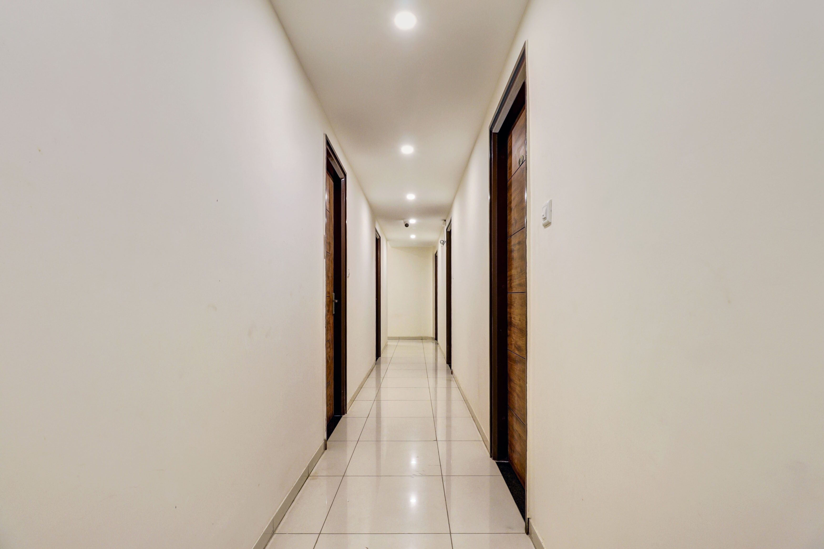 A long, narrow hallway with white walls and a tiled floor, leading to a door at the end.