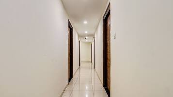 A long, narrow hallway with white walls and a tiled floor, leading to a door at the end.