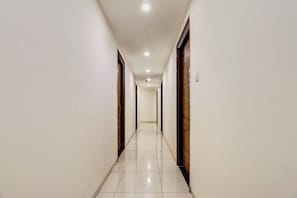Un pasillo largo y estrecho con paredes blancas y piso de baldosas, que conduce a una puerta al final.