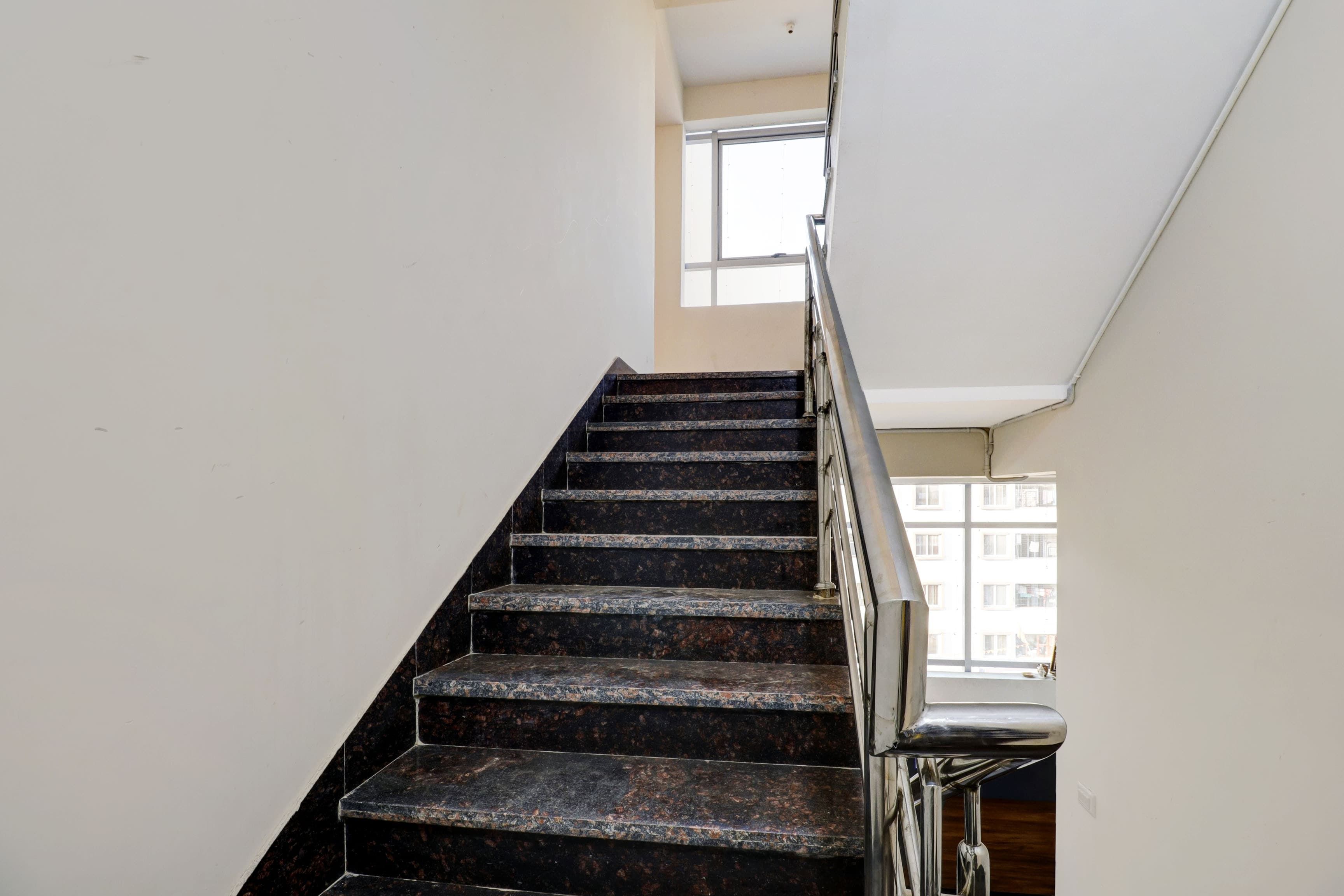 A staircase with dark marble steps and a metal handrail, leading to a landing with a window.