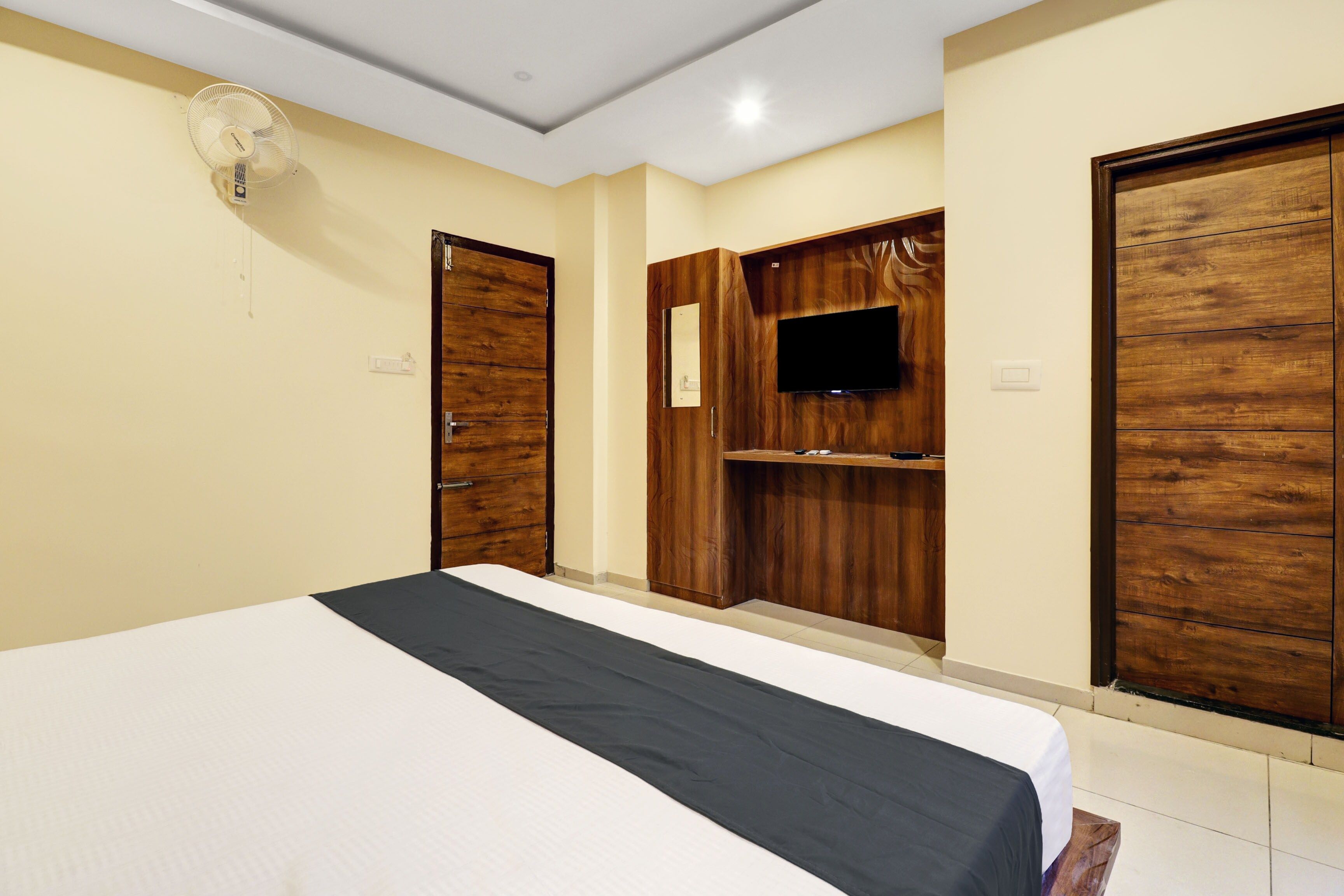 A hotel room with a bed, wooden wardrobe, a flat-screen TV, and a ceiling fan.