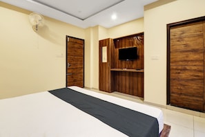 A hotel room with a bed, wooden wardrobe, a flat-screen TV, and a ceiling fan.