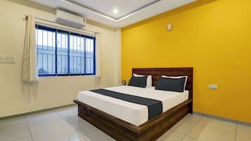 A hotel room with a bed, a window with bars, an air conditioning unit, and a yellow wall.