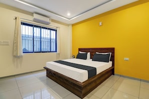 Habitación de hotel con cama, ventana con barrotes, unidad de aire acondicionado y pared amarilla.