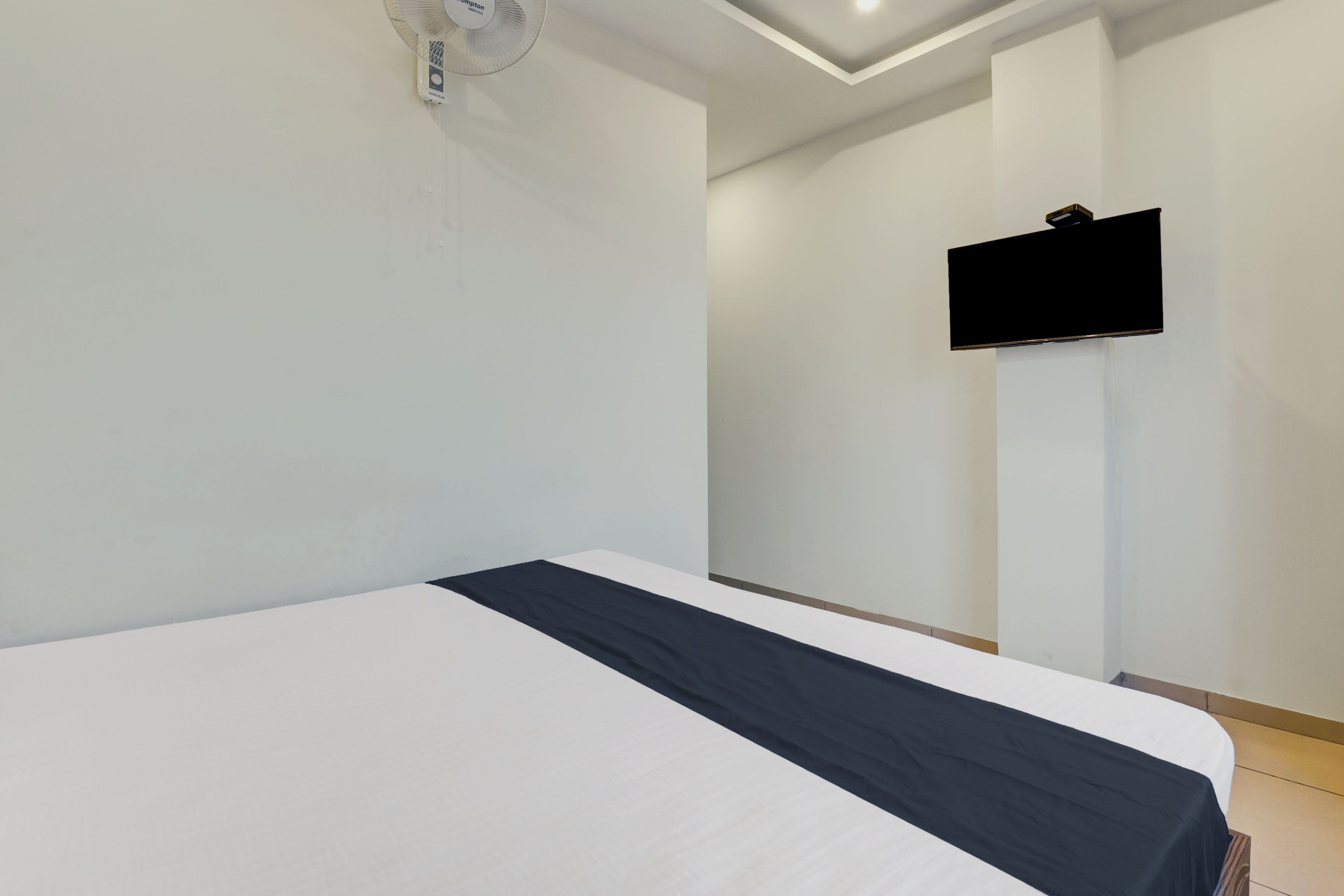 Habitación de hotel con cama, televisor montado en la pared y ventilador de techo.